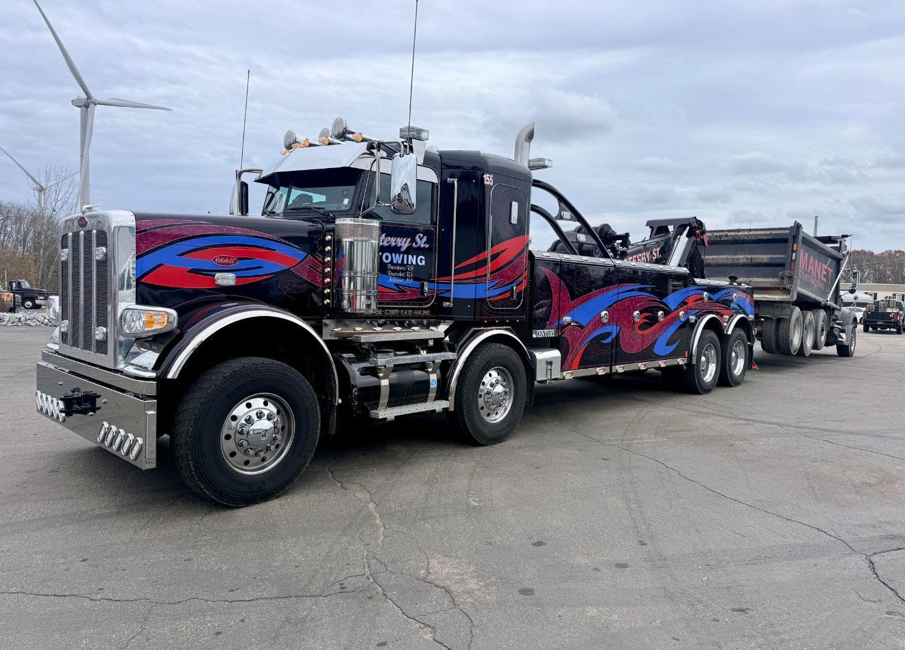 Custom black semi-truck with red and blue graphics parked on a lot, towing another truck.