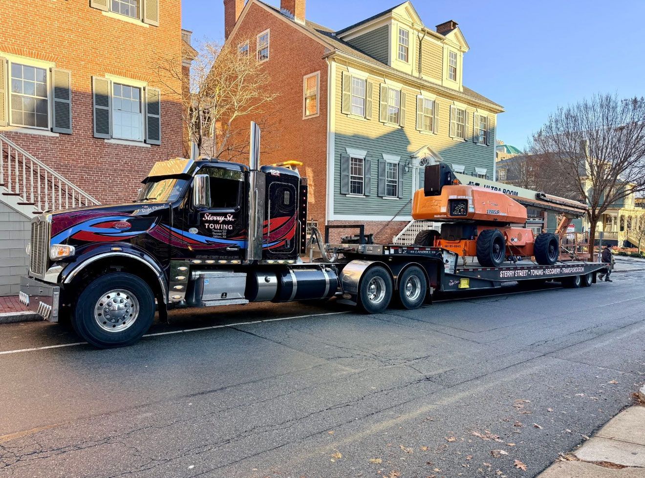 Tow truck hauling a black SUV on a flatbed trailer along a residential street.