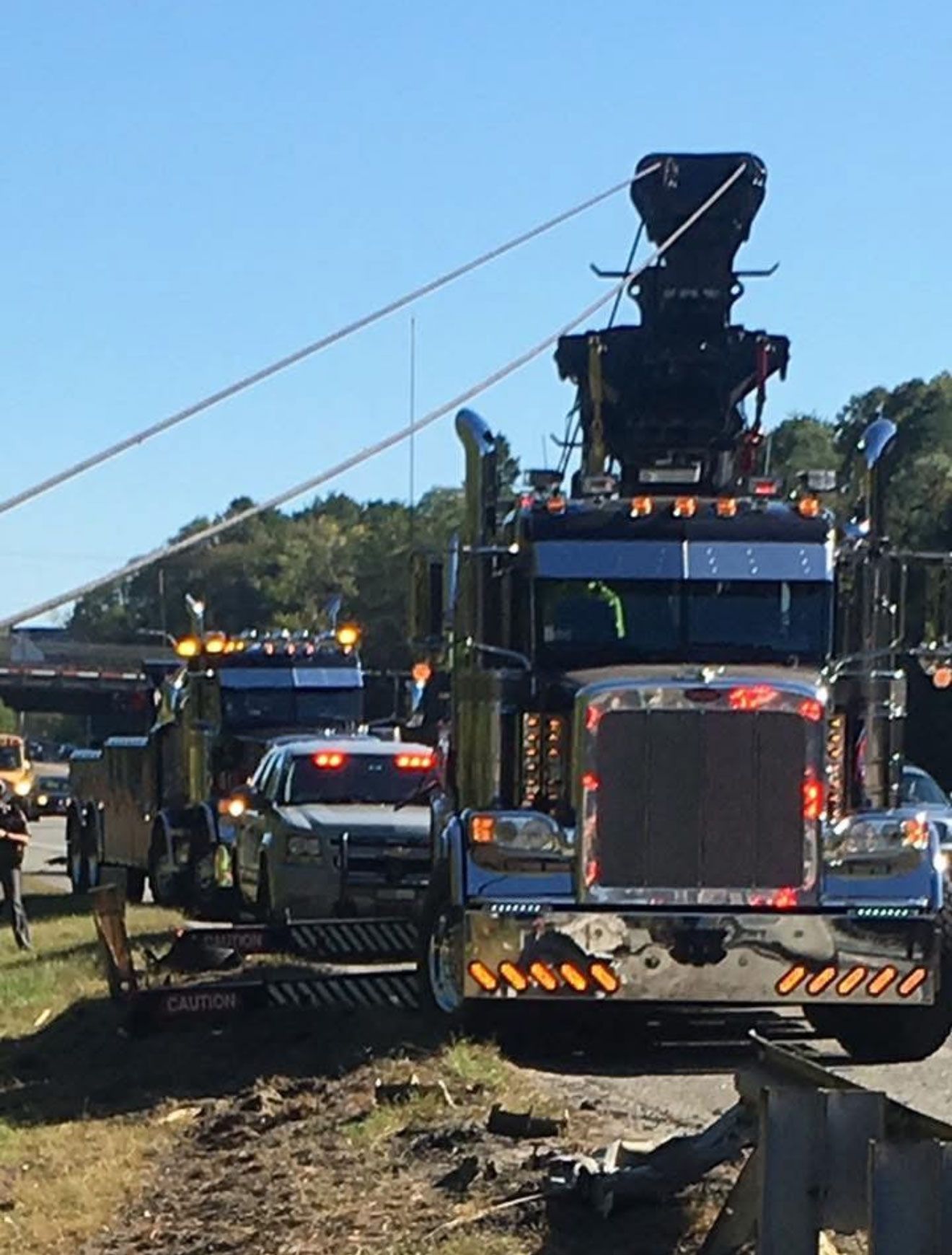 Tow truck convoy on a dirt road, with a large black recovery truck in front under a blue sky.