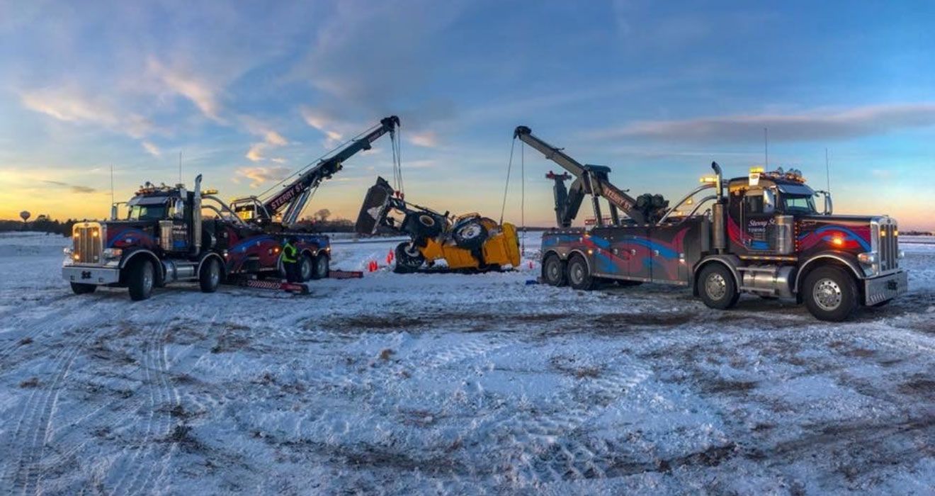 Snowy worksite with three red heavy trucks and raised booms at sunset.