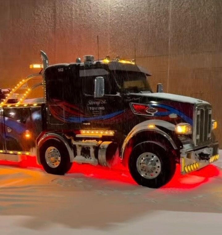 Black semi-truck with red underglow driving through snow at night.