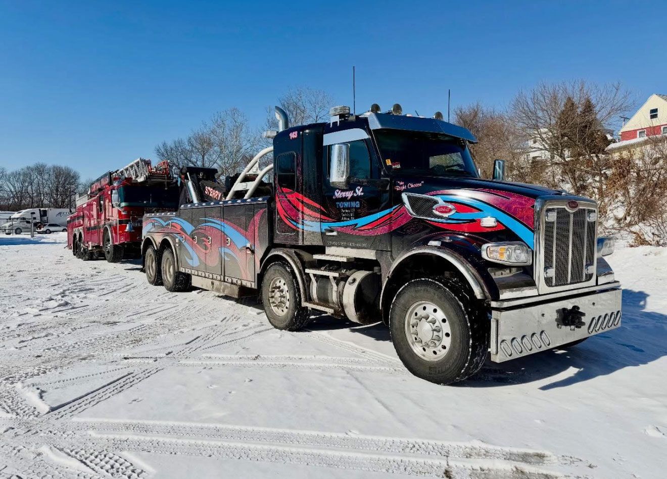 Colorfully wrapped semi trucks lined up on a snowy road under a clear blue sky.