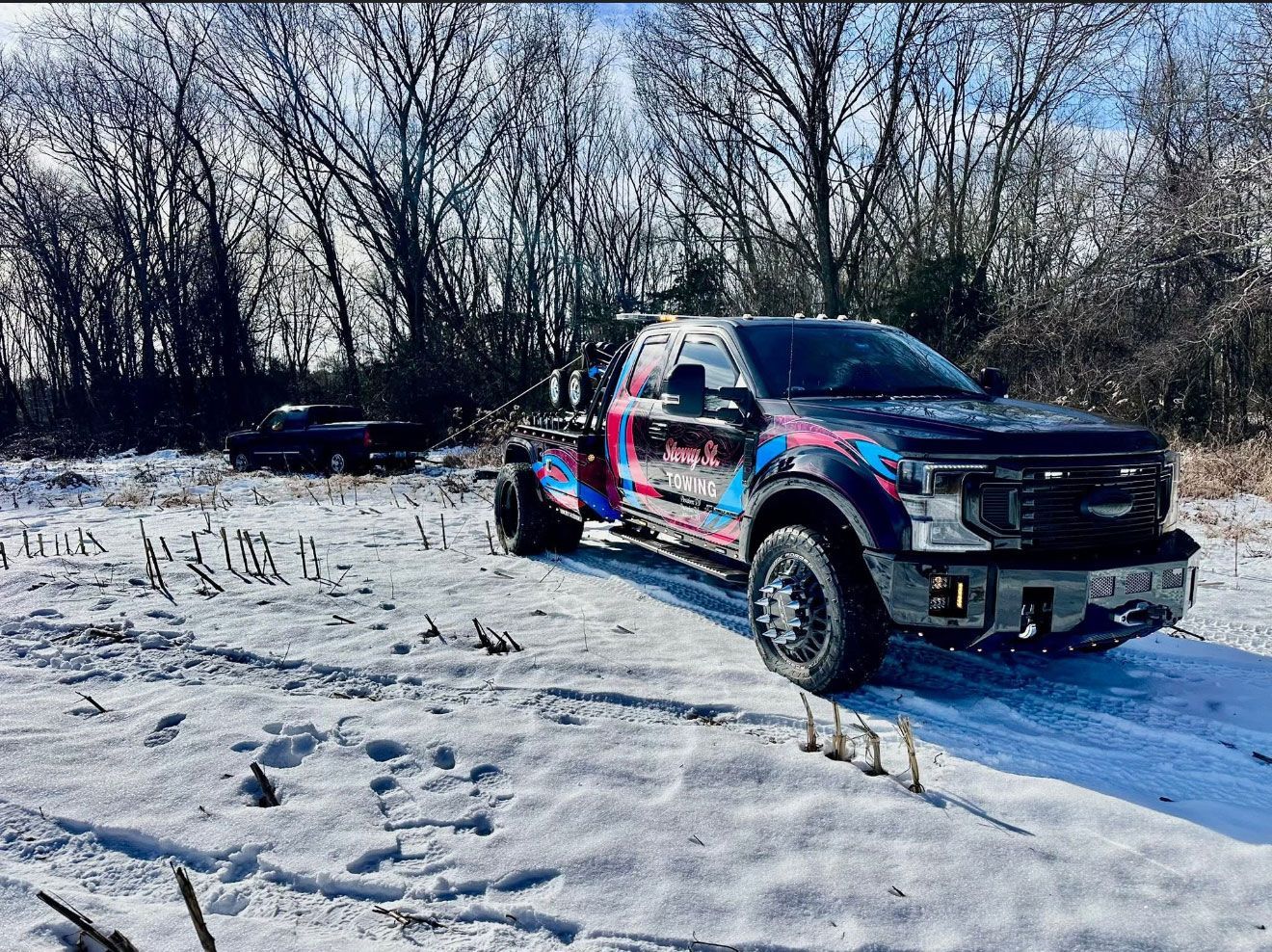 Black pickup truck with colorful decals parked on a snowy road beside leafless trees.