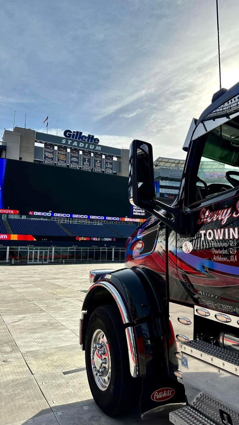 Truck parked in a stadium lot with a large scoreboard and stands in the background.