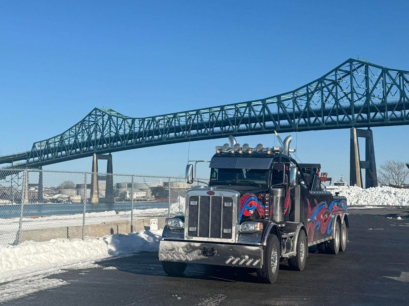 Decorated semi-truck parked near a large steel bridge on a snowy day.