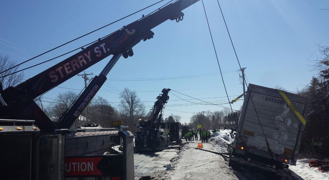 Crane lifts a damaged utility truck on a snowy street with downed power lines blocking the road.