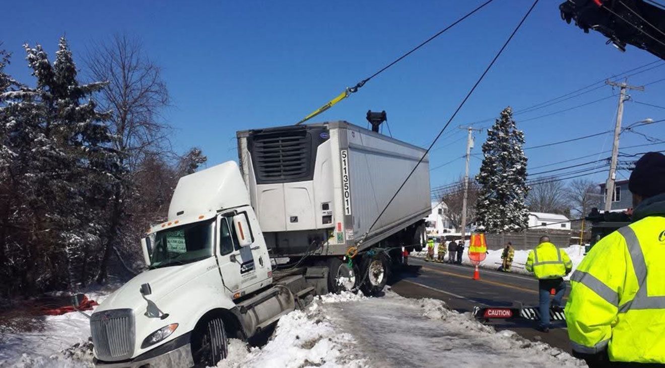 Semi-truck crashed into snowbank on a snowy roadside, with emergency workers nearby.