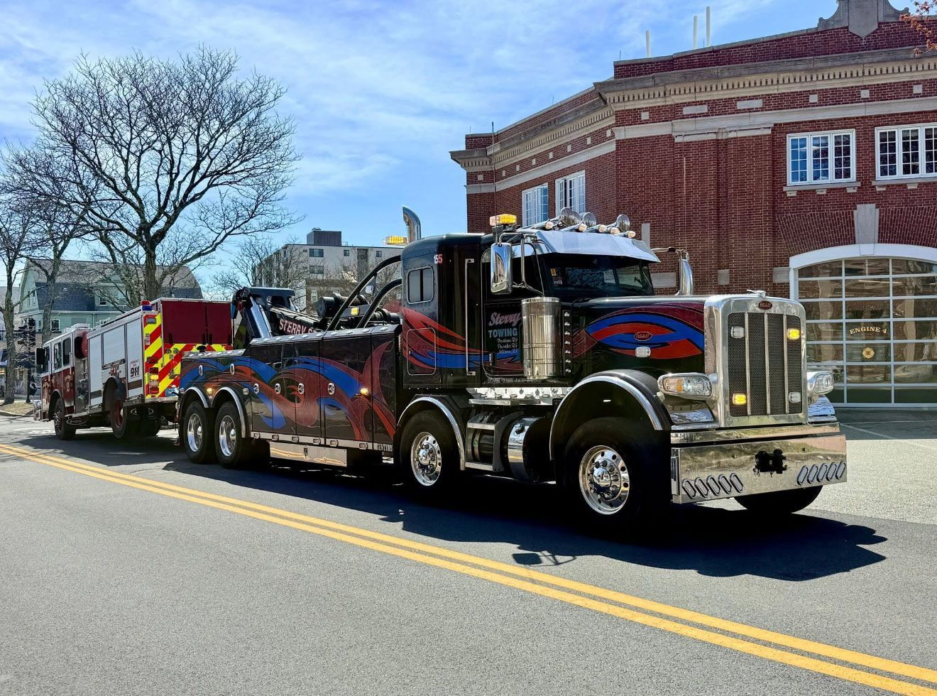 Custom chrome semi-truck parked on a street beside a brick building, with a tow truck behind it.