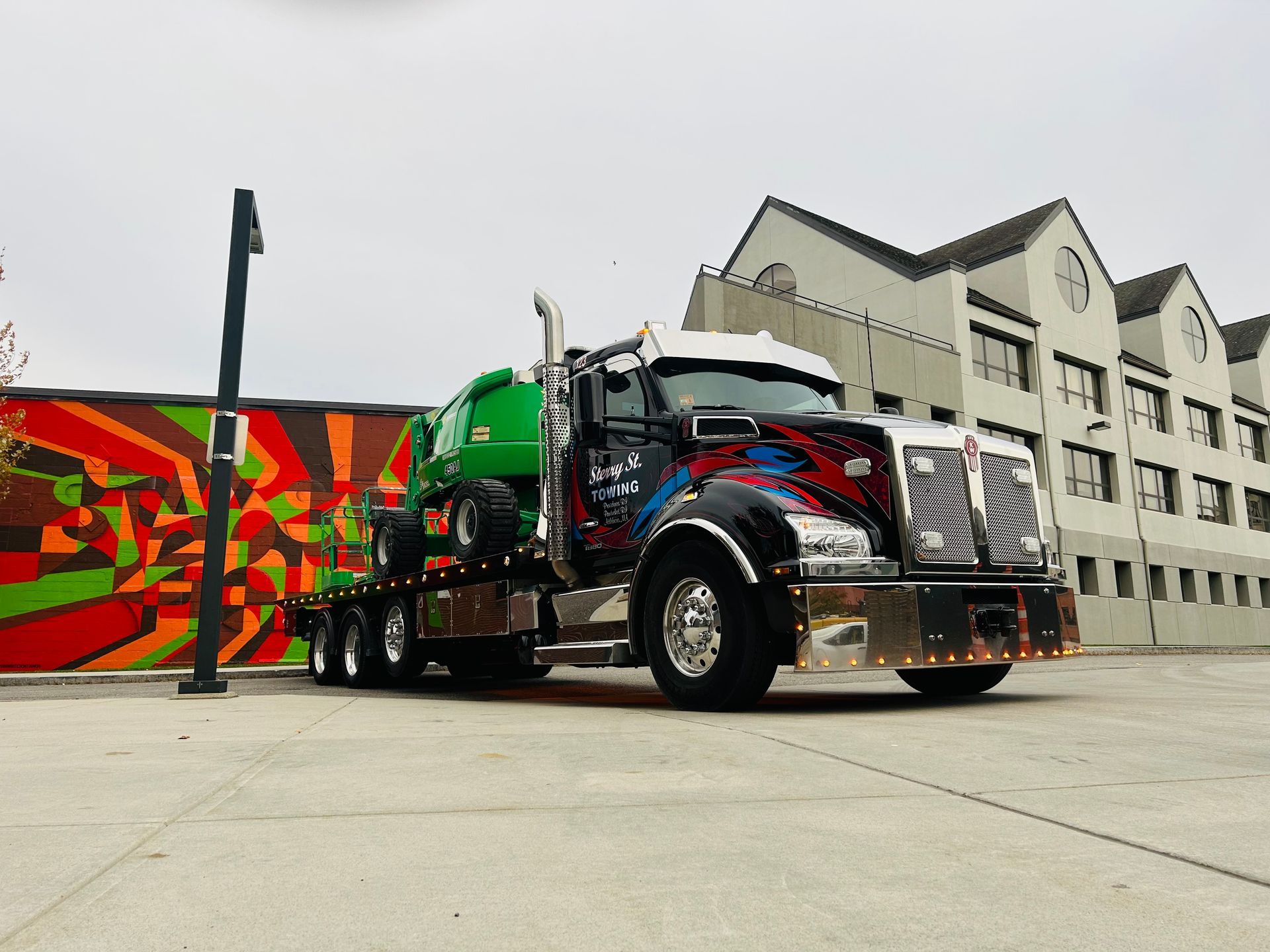 Colorful semi truck parked in front of a building with a mural on the left.