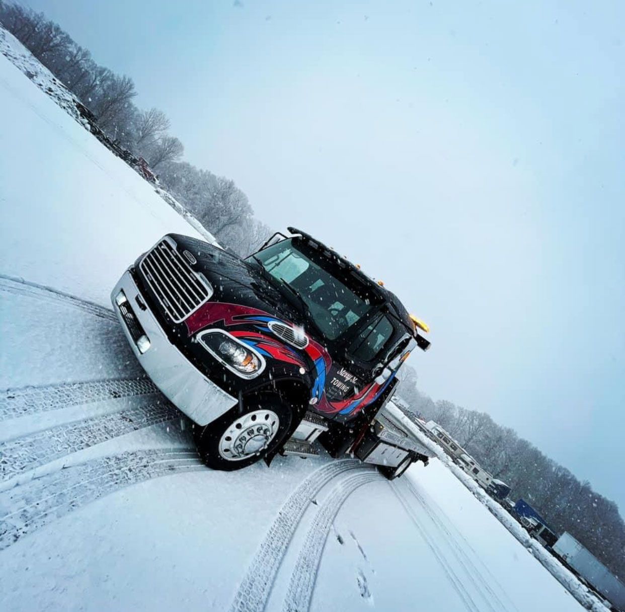 Red tow truck pulling a maroon car on a snowy road, with tire tracks visible.