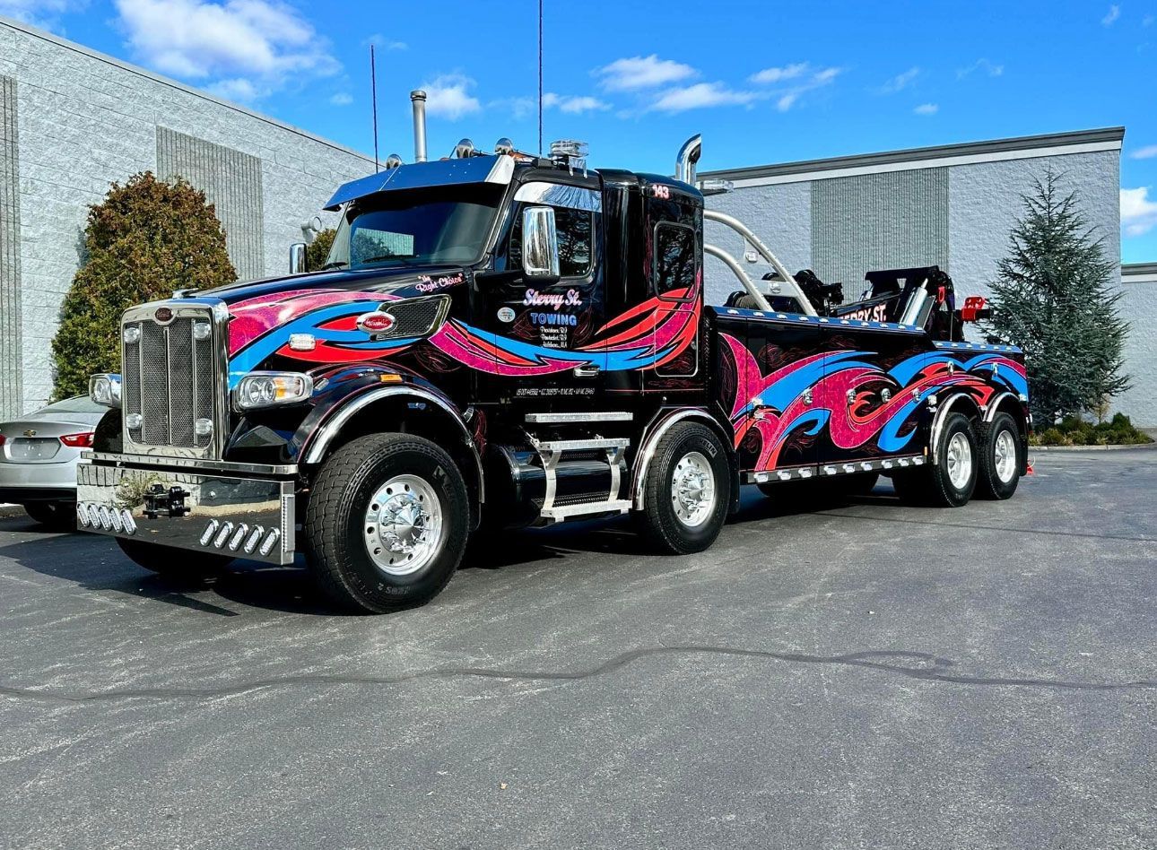 Custom black, pink, and blue tow truck parked outdoors on a sunny day.