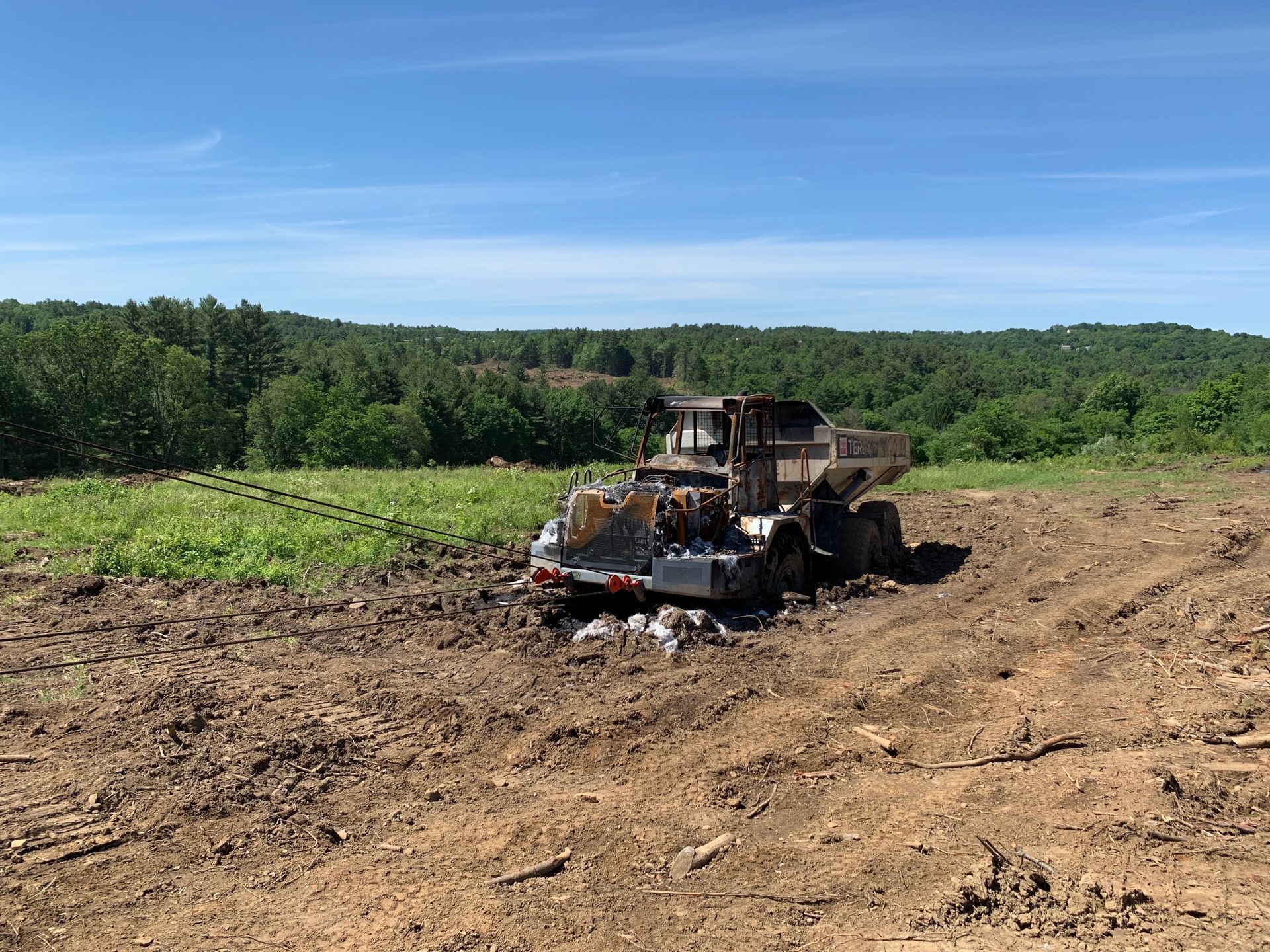 Bulldozer clearing a dirt field under a blue sky, with green trees in the background.