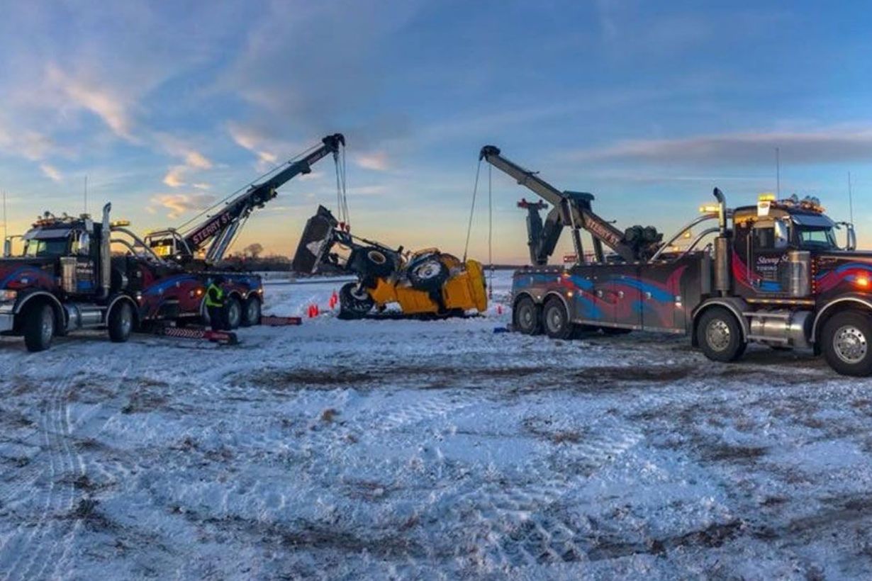 Heavy rescue trucks and cranes at a snowy roadside scene at dusk