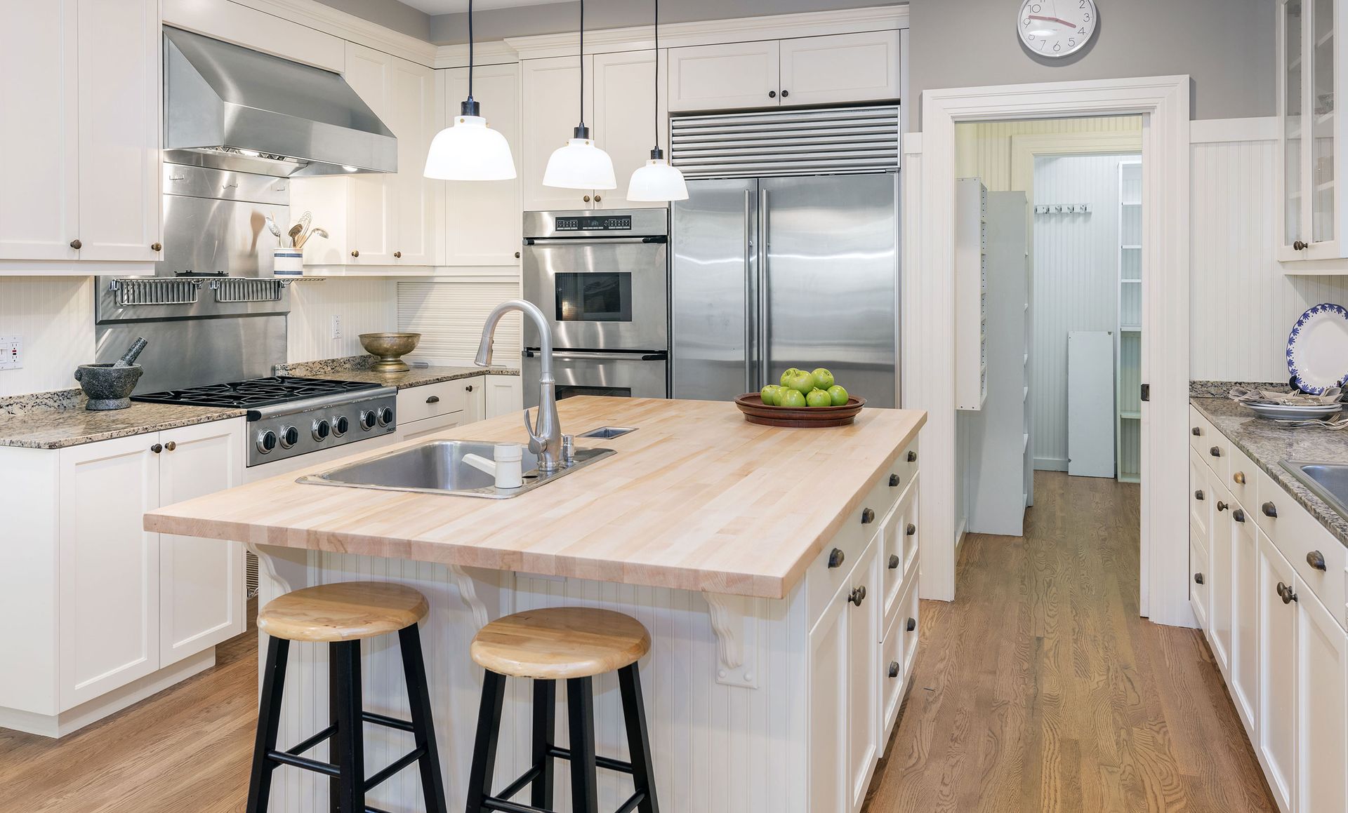 A kitchen with white cabinets, wooden counter tops, stainless steel appliances and a large island