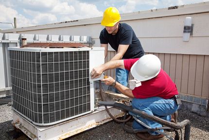 Two workers in hard hats repairing a rooftop HVAC unit outdoors