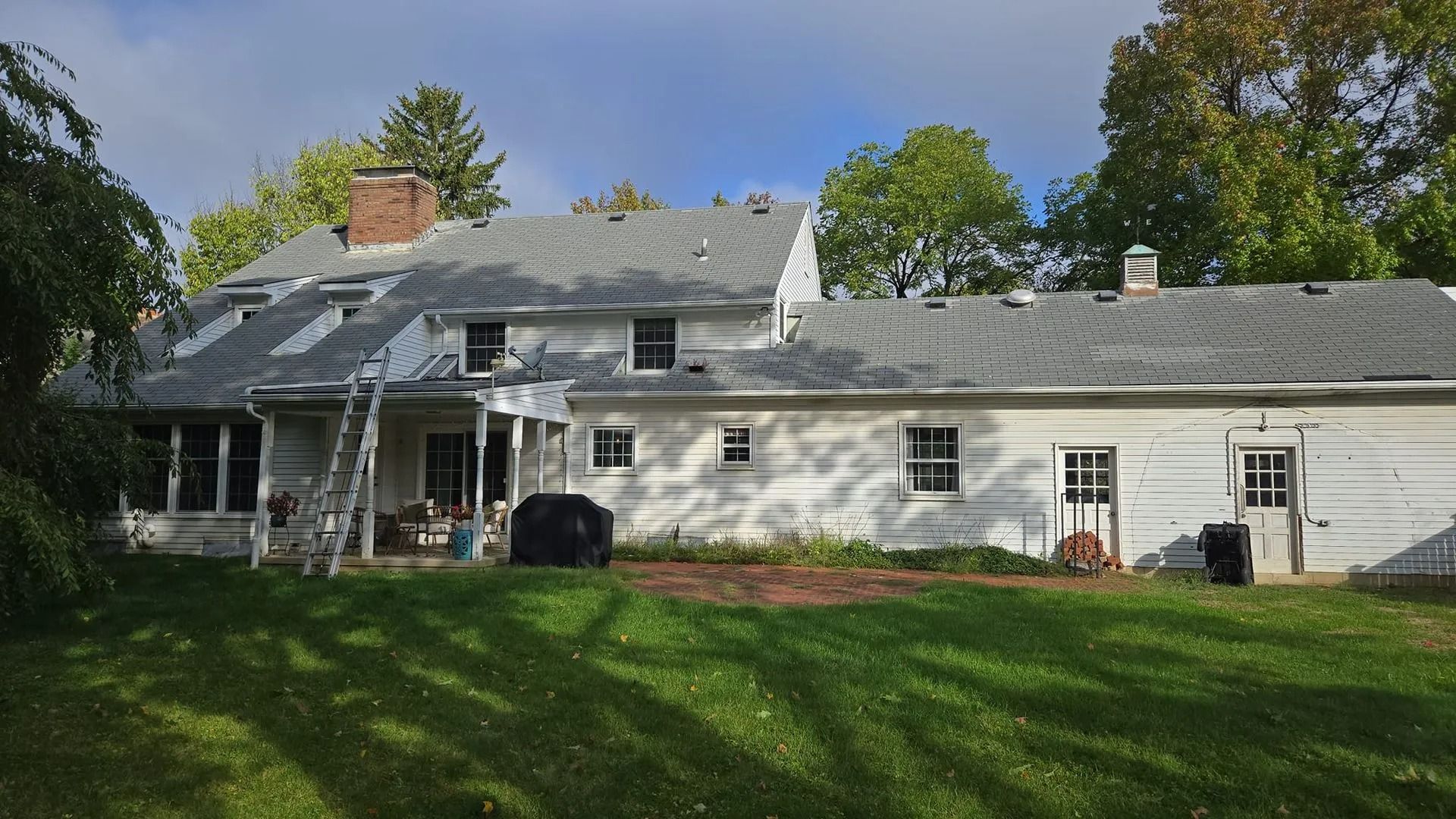 Back view of a two-story white house with gray roof; ladder leans against the side; green lawn.