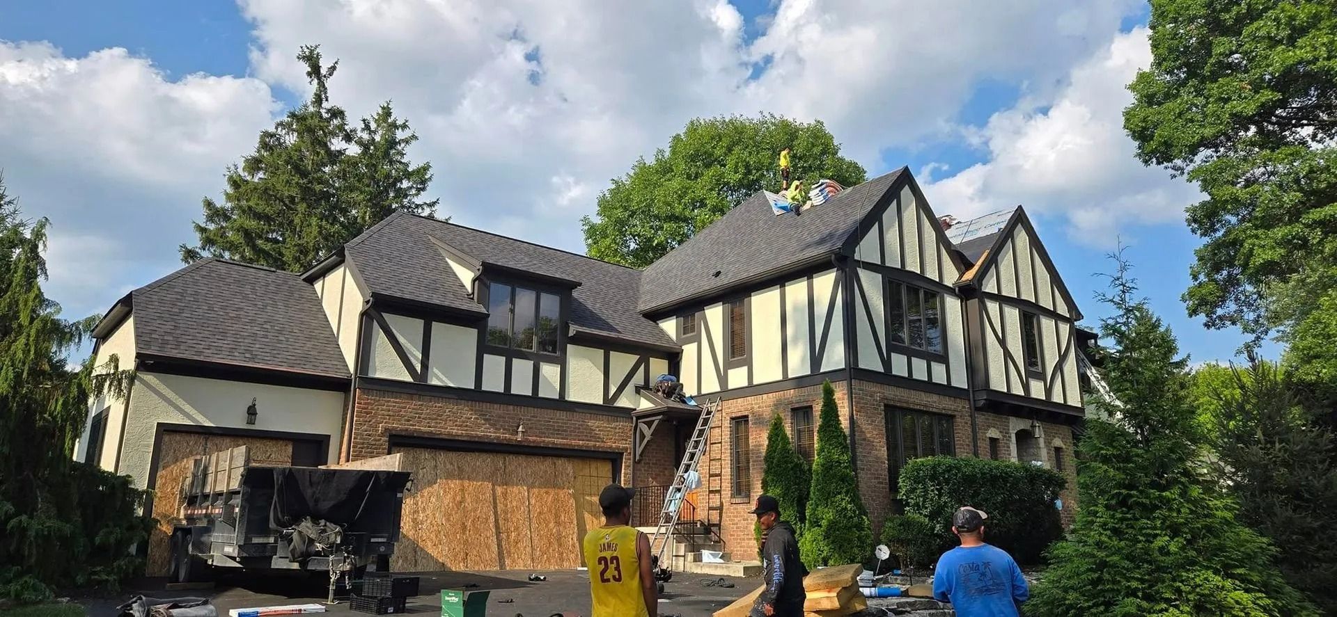 Tudor style house with black roof and white and black trim. People and construction equipment.