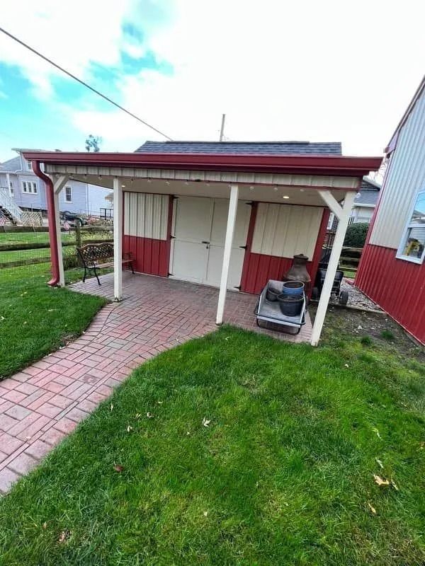 Red and white shed with brick walkway, sitting on a green lawn with a white and red building to the right.