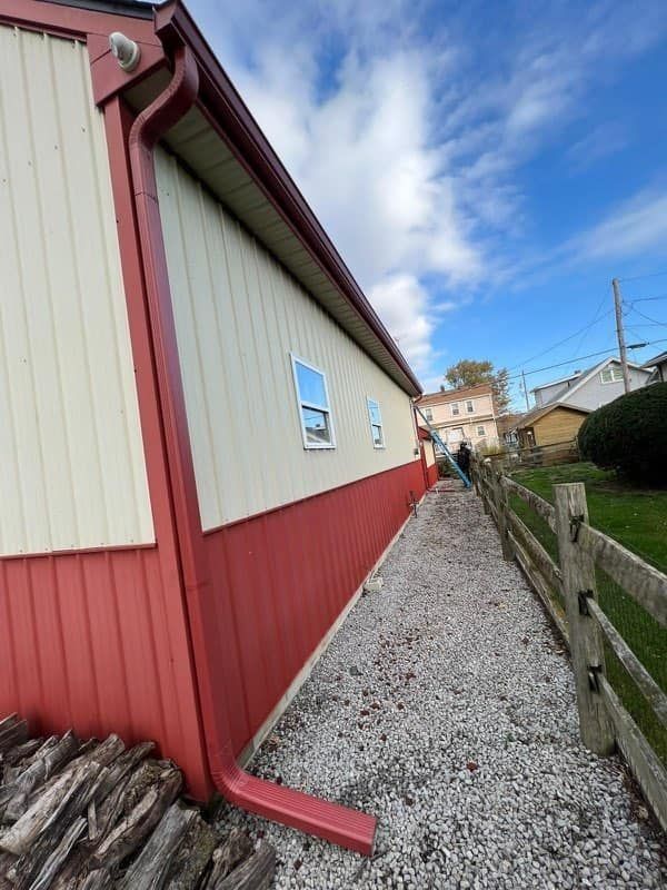 Side view of a building with red and beige siding, with a gravel path and wooden fence.
