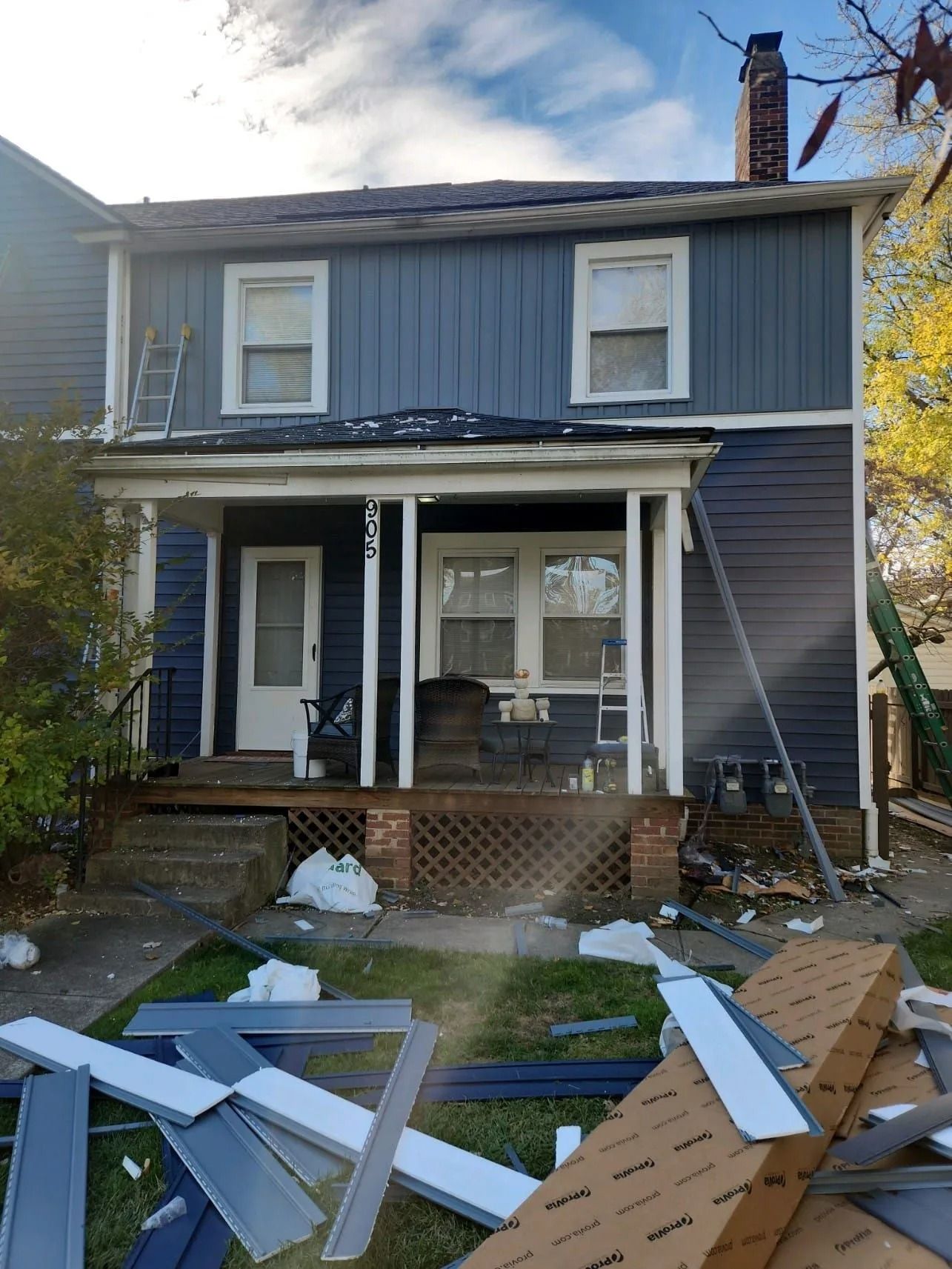 Two-story house with blue siding, a porch, and construction materials on the ground.