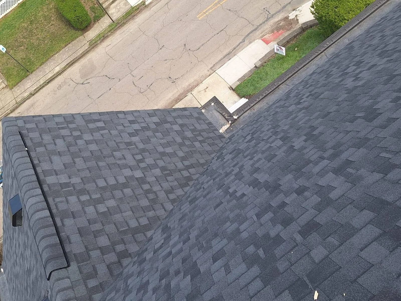 Overhead view of a dark gray shingle roof. Street and sidewalk visible behind the roof.