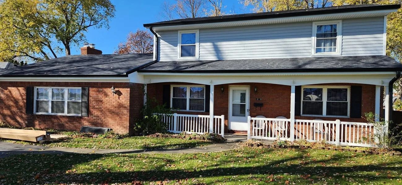A two-story brick and siding house with a porch, surrounded by grass and trees.