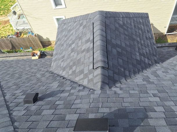 A gray shingle roof with a dormer, two vents, and part of a house and fence in the background.