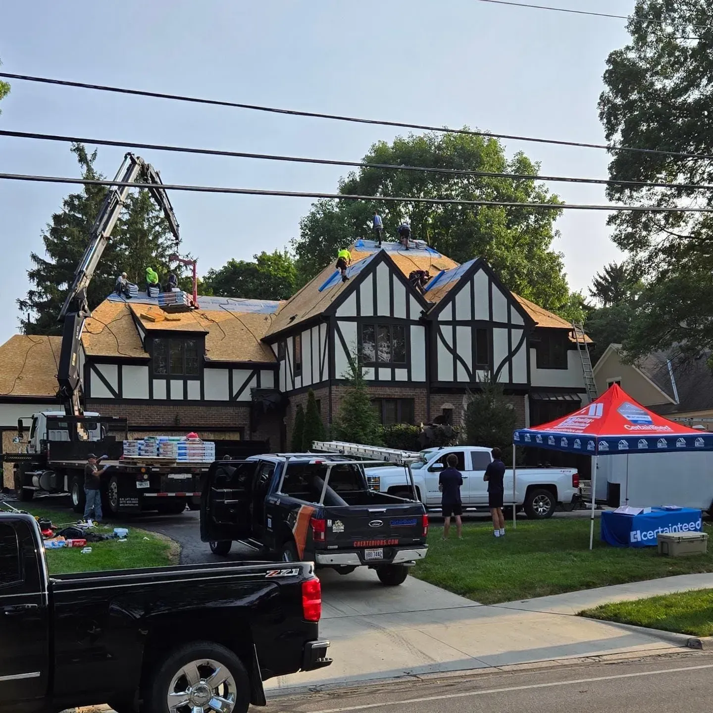 Roofers working on a Tudor-style house; truck and crane visible in the yard.
