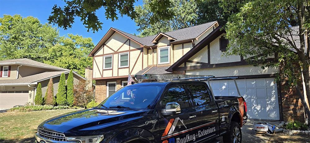 Black truck parked in front of a beige and brown house with trees.