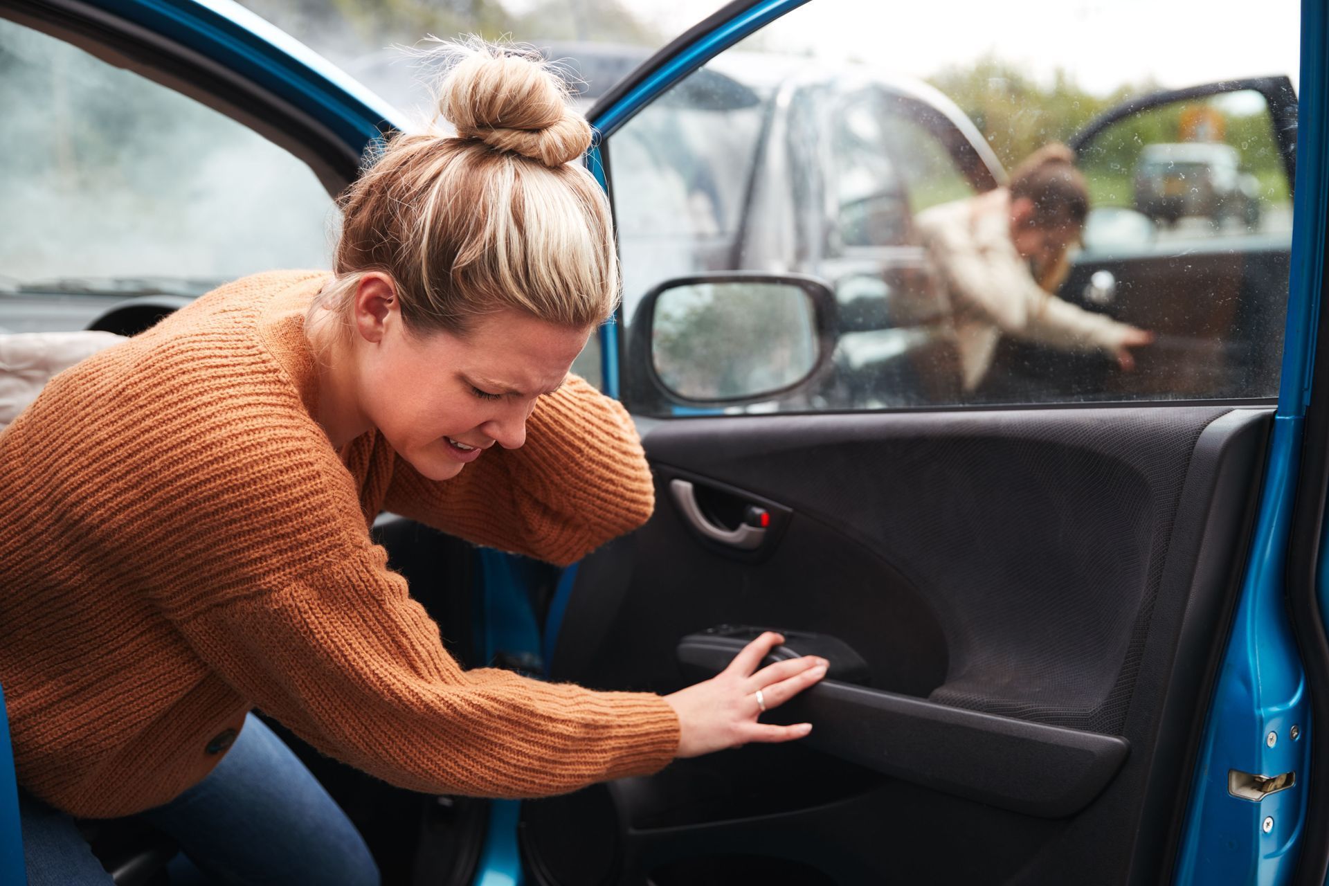 Woman opening a blue car door while reaching inside, with a child visible in the back seat.
