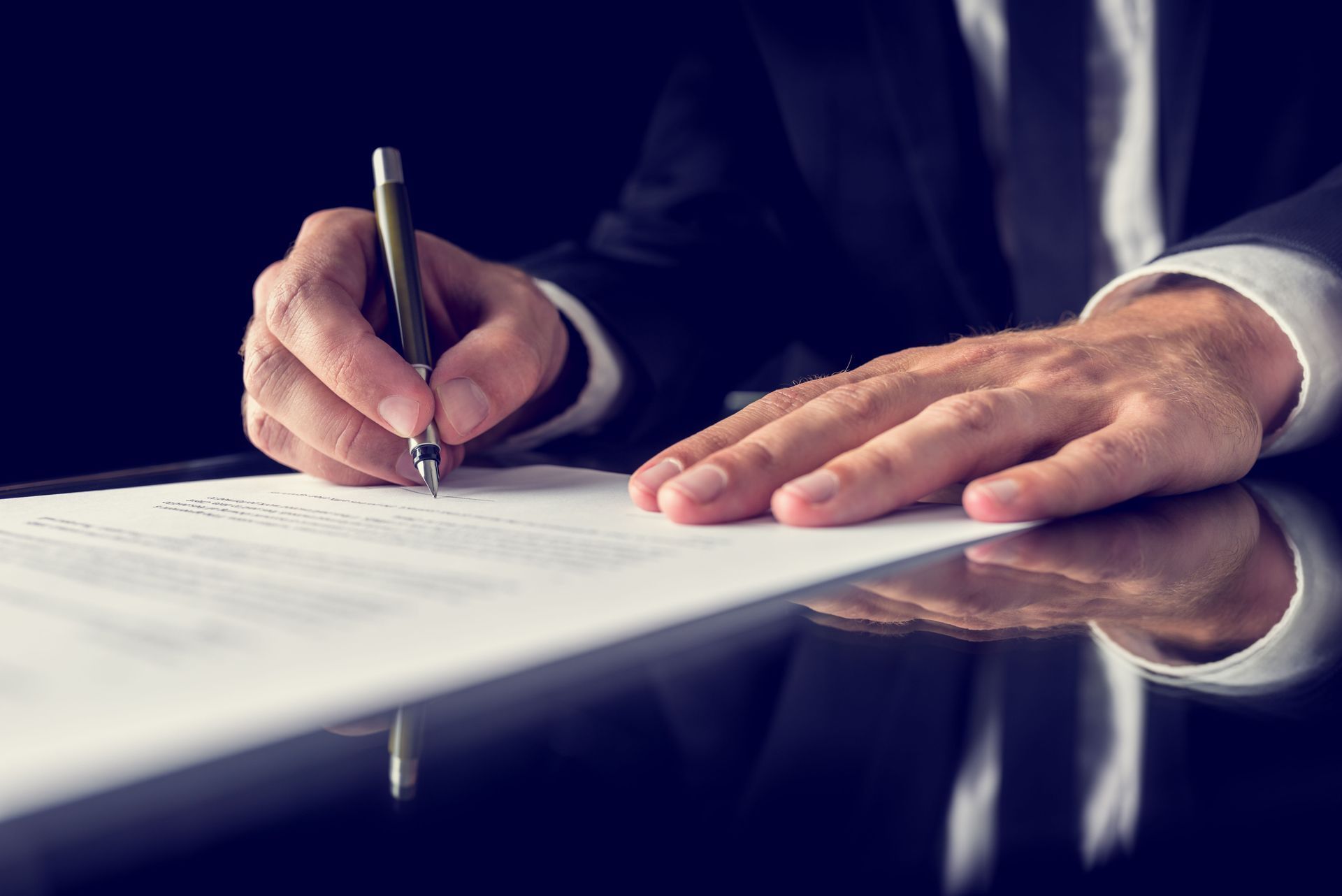Businessperson signing a document with a pen at a desk, close-up with hands visible.