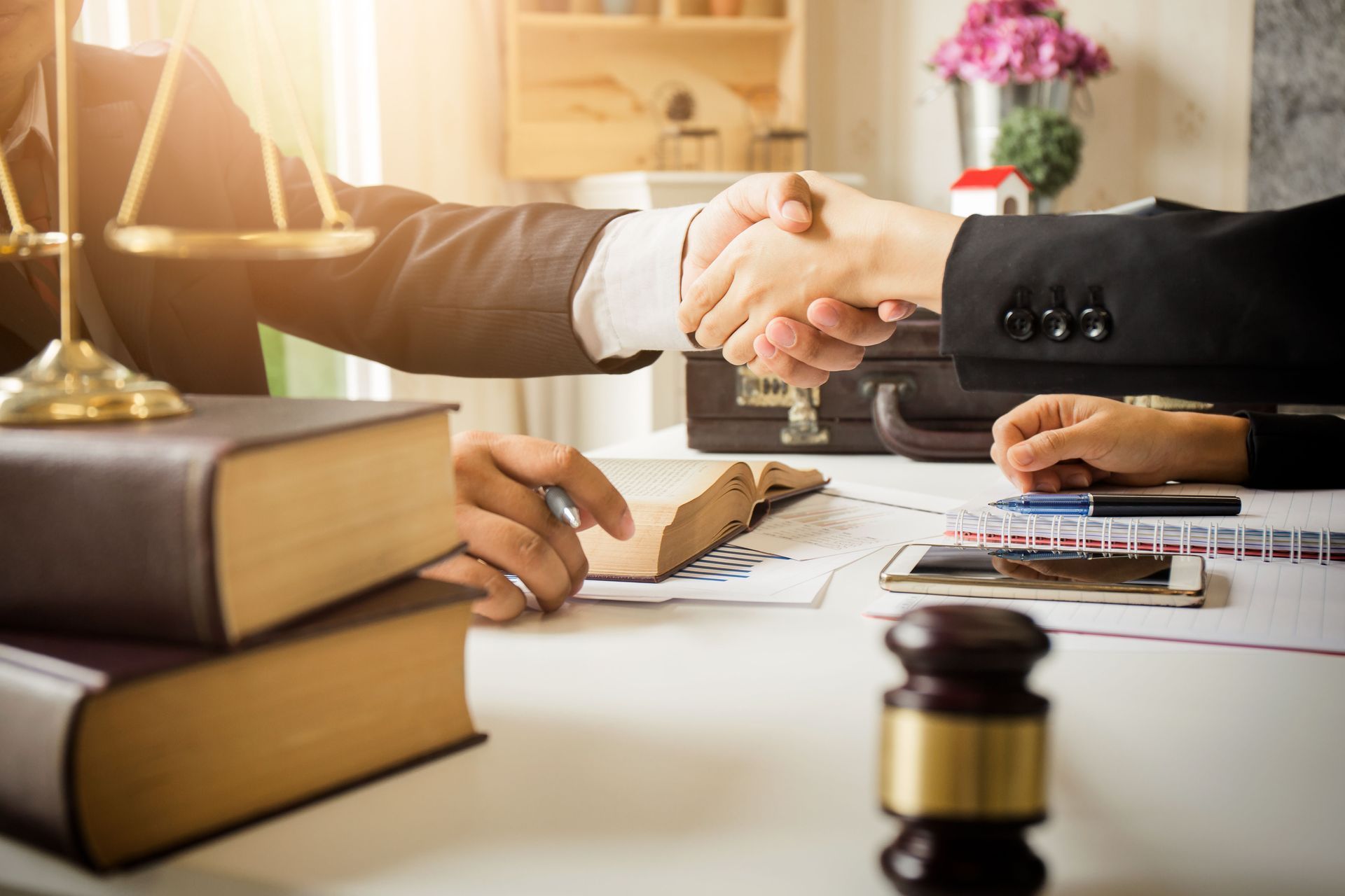 Two people shaking hands across a desk with legal documents and a gavel in a law office