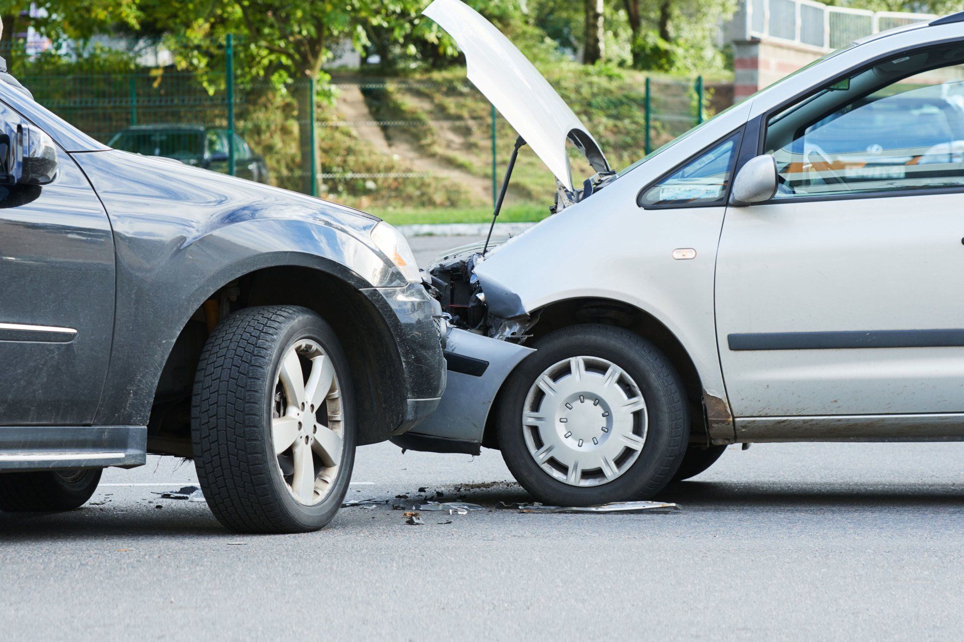 Two cars with front-end collision, white car hood open and gray car damaged on a street