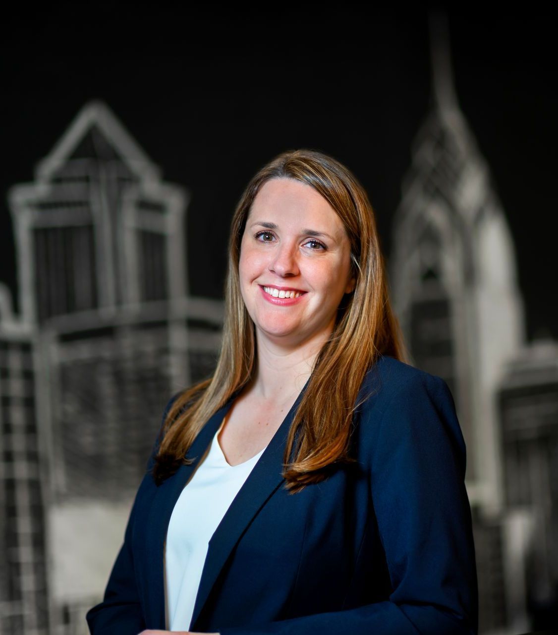 Woman in a navy blazer smiling in front of a black-and-white city skyline mural
