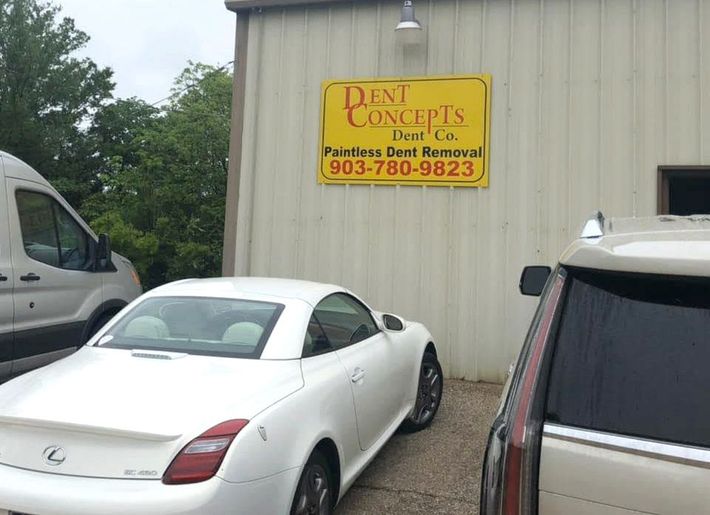 A white car is parked in front of a building that says dent concepts