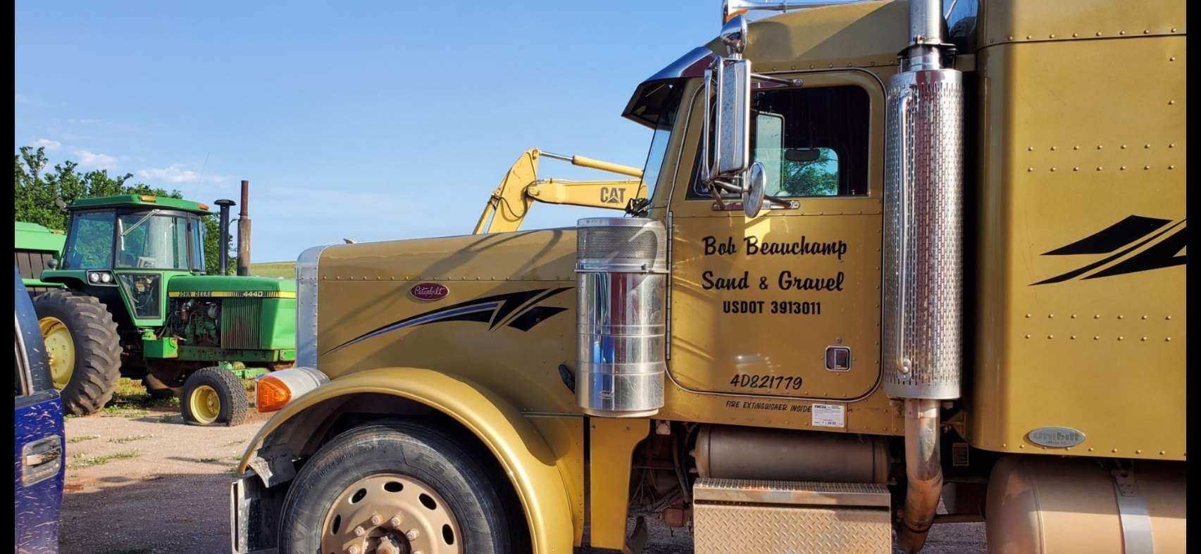 A yellow semi truck is parked next to a green tractor.