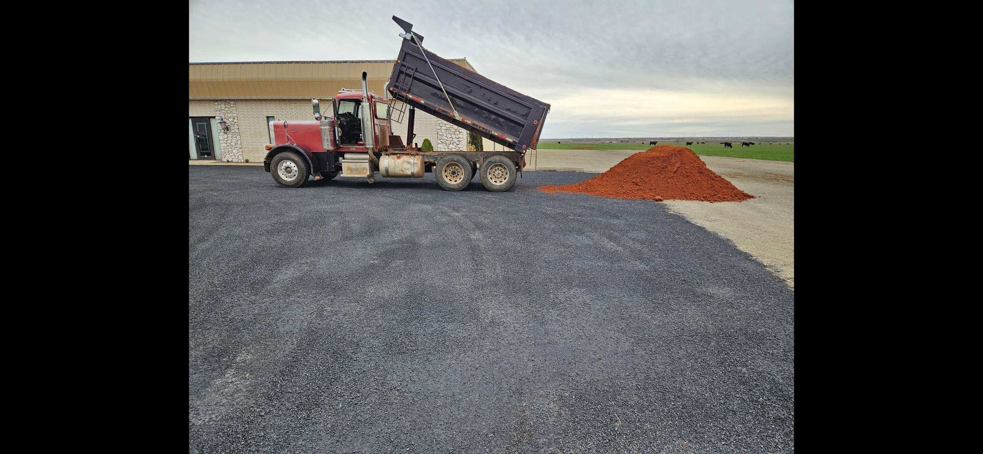 A dump truck is dumping dirt into a gravel driveway.