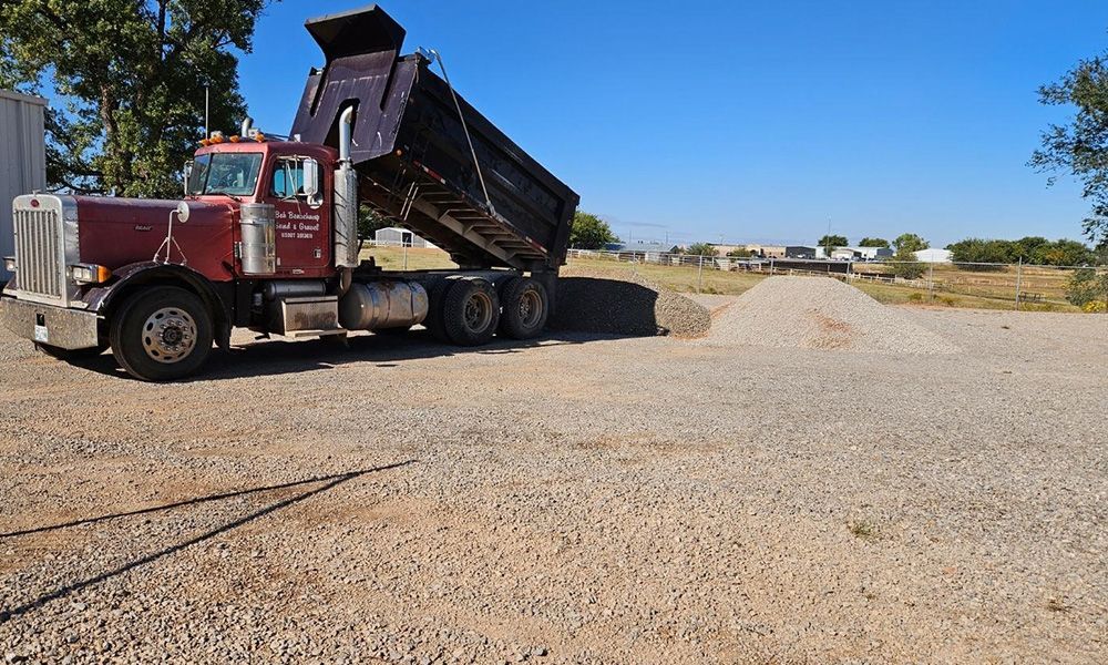 A red dump truck is parked in a gravel lot