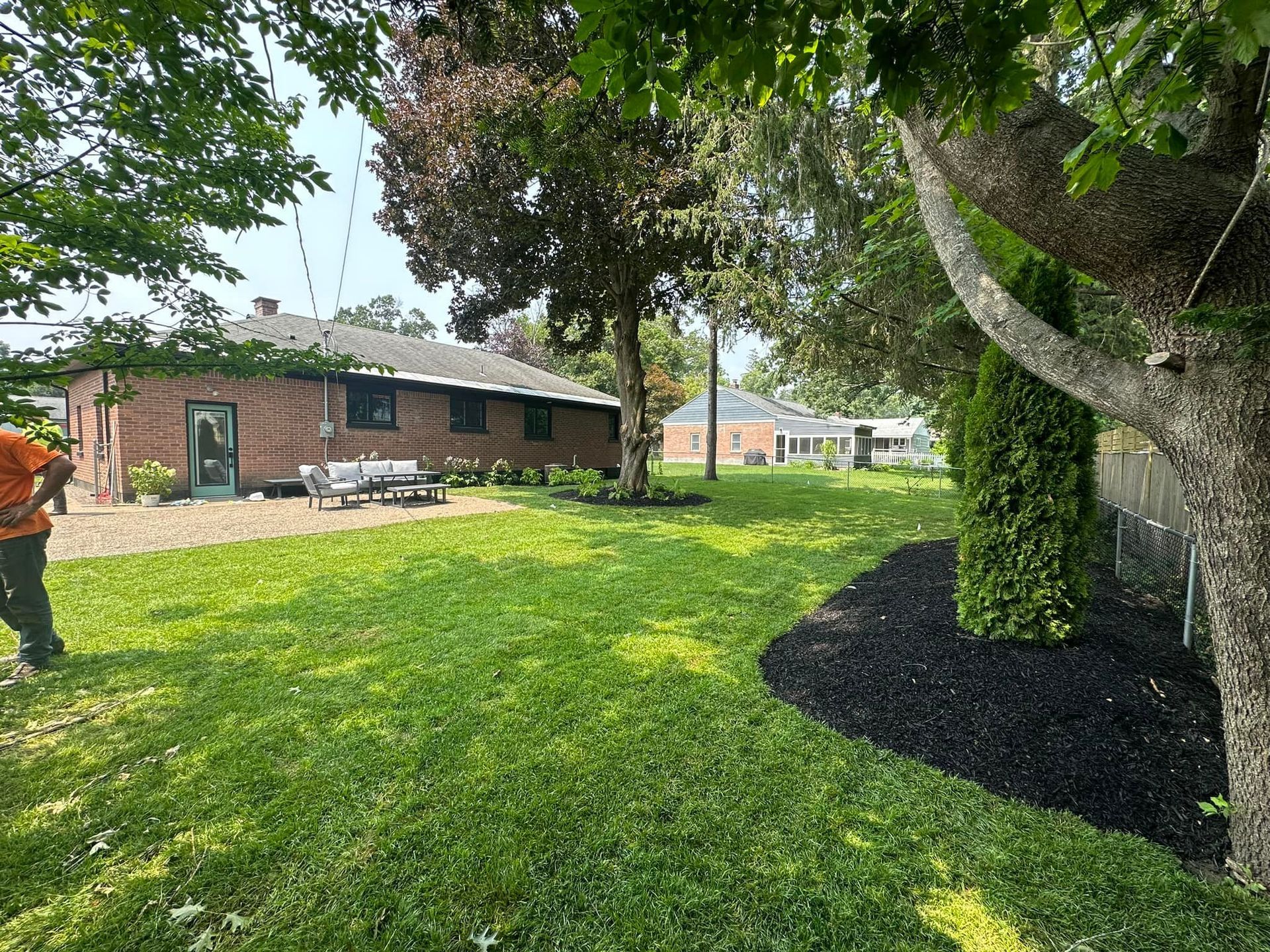 A man is mowing the lawn in front of a brick house.