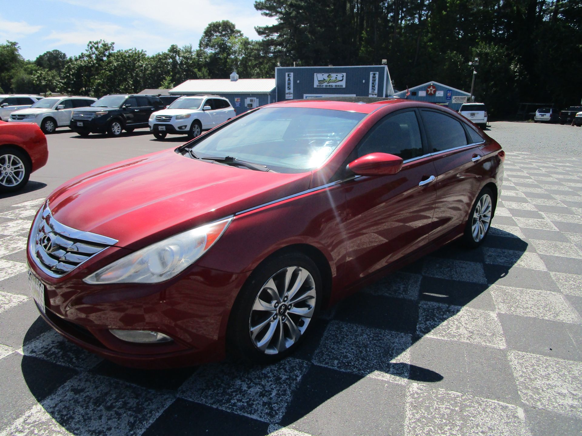 Red sedan parked in a lot on a sunny day with other vehicles in the background