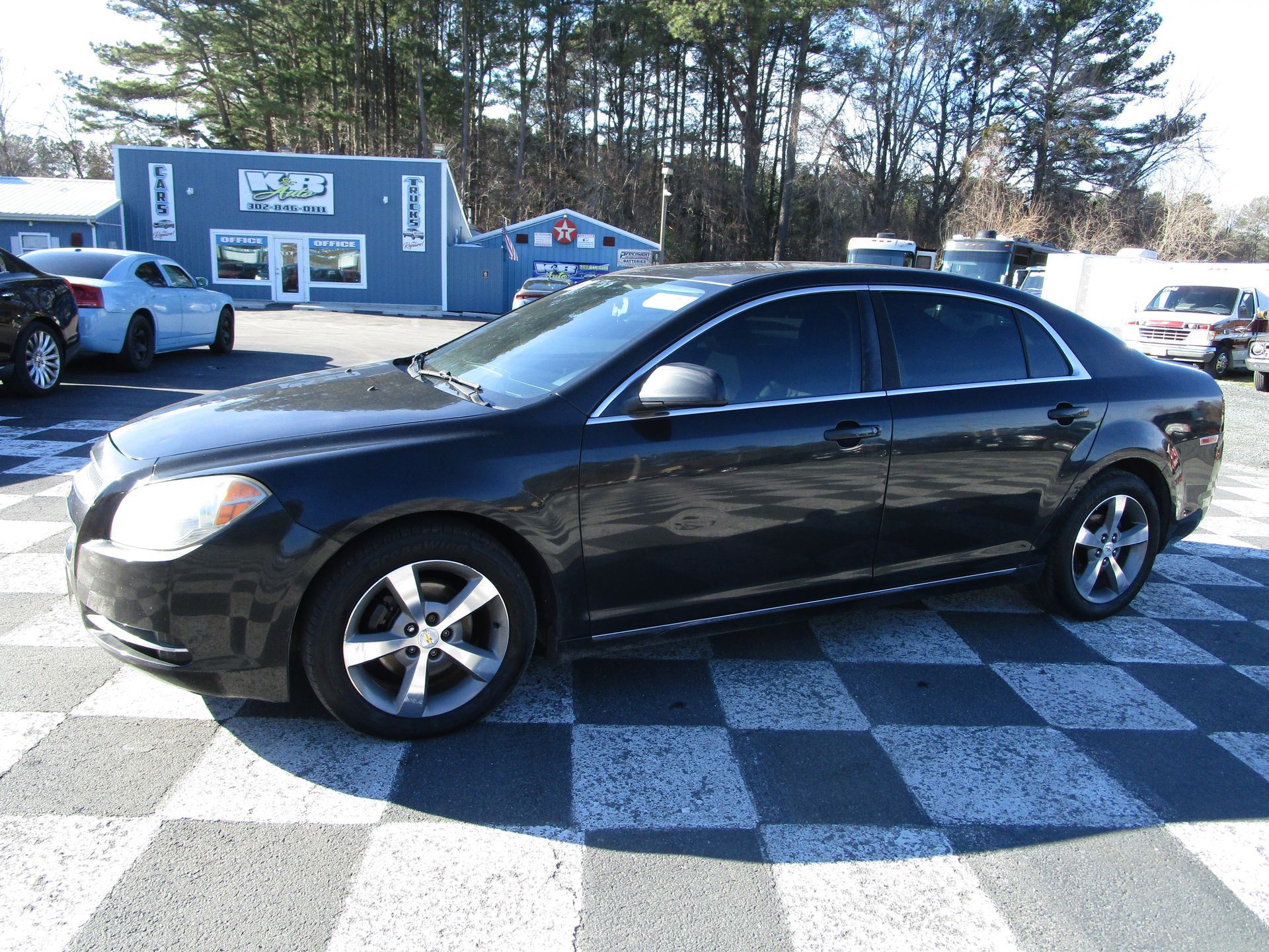 Black Chevrolet Malibu parked in a lot with a building and other cars in the background.