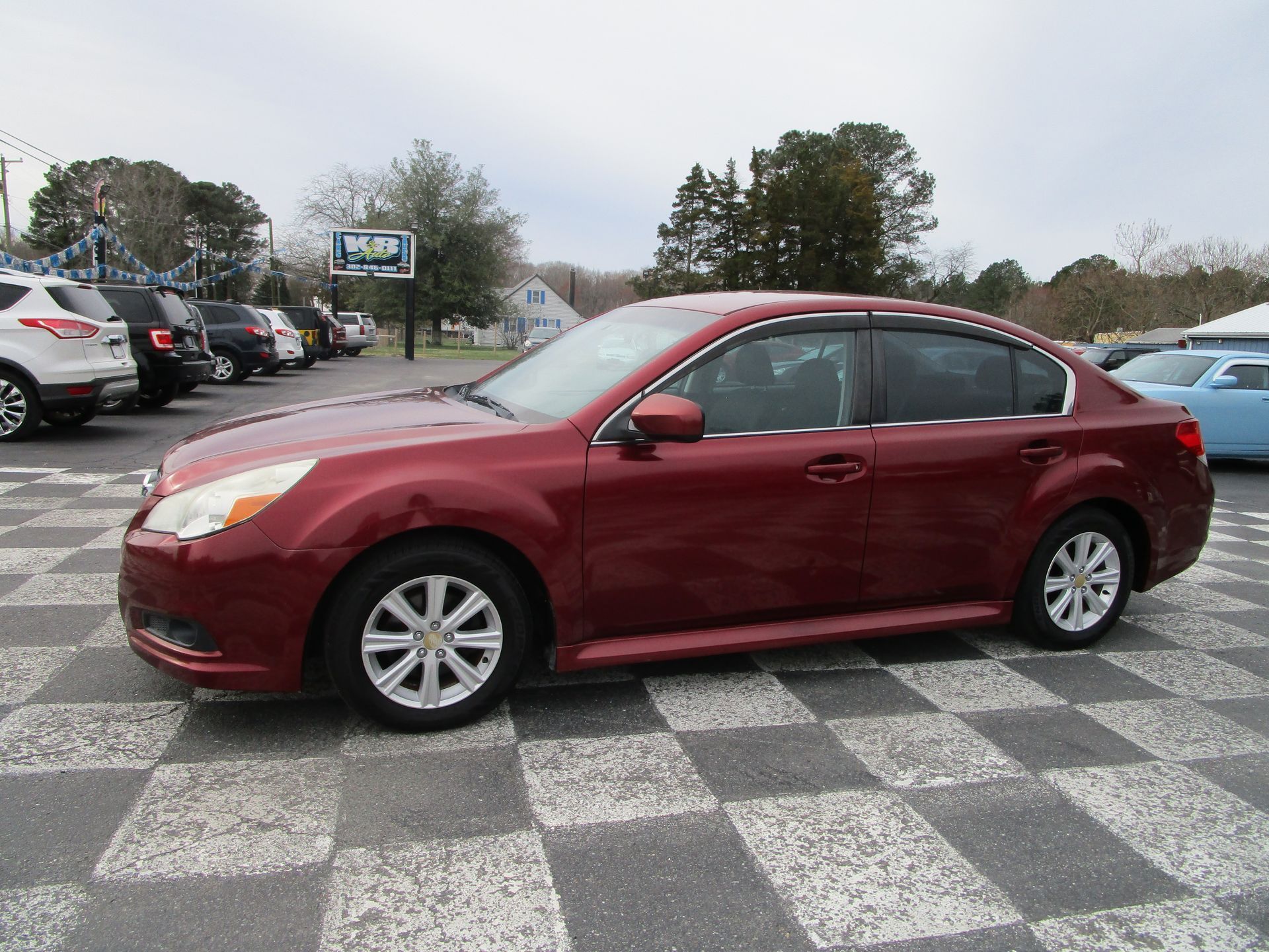 A maroon mid-size sedan parked on a checkered lot at a car dealership on an overcast day.