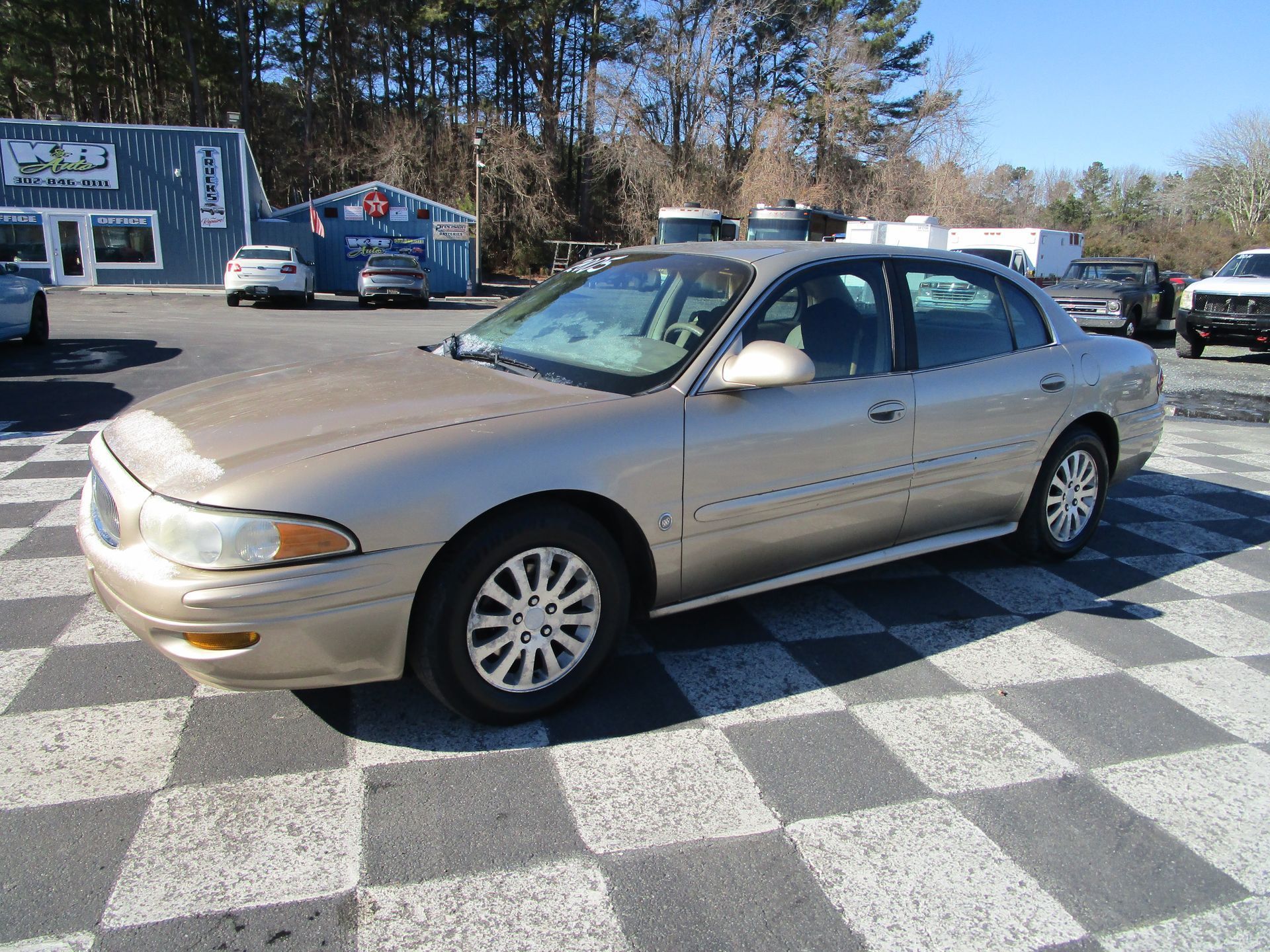 Gold Buick sedan parked in a lot with a checkered pattern pavement, sunny day.