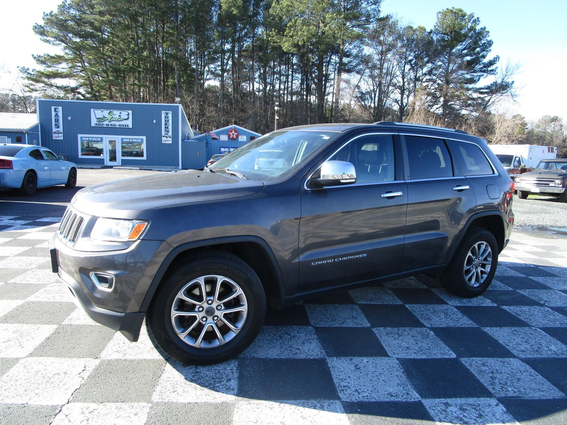 Dark gray Jeep Grand Cherokee parked on a checkered lot in front of a blue building.