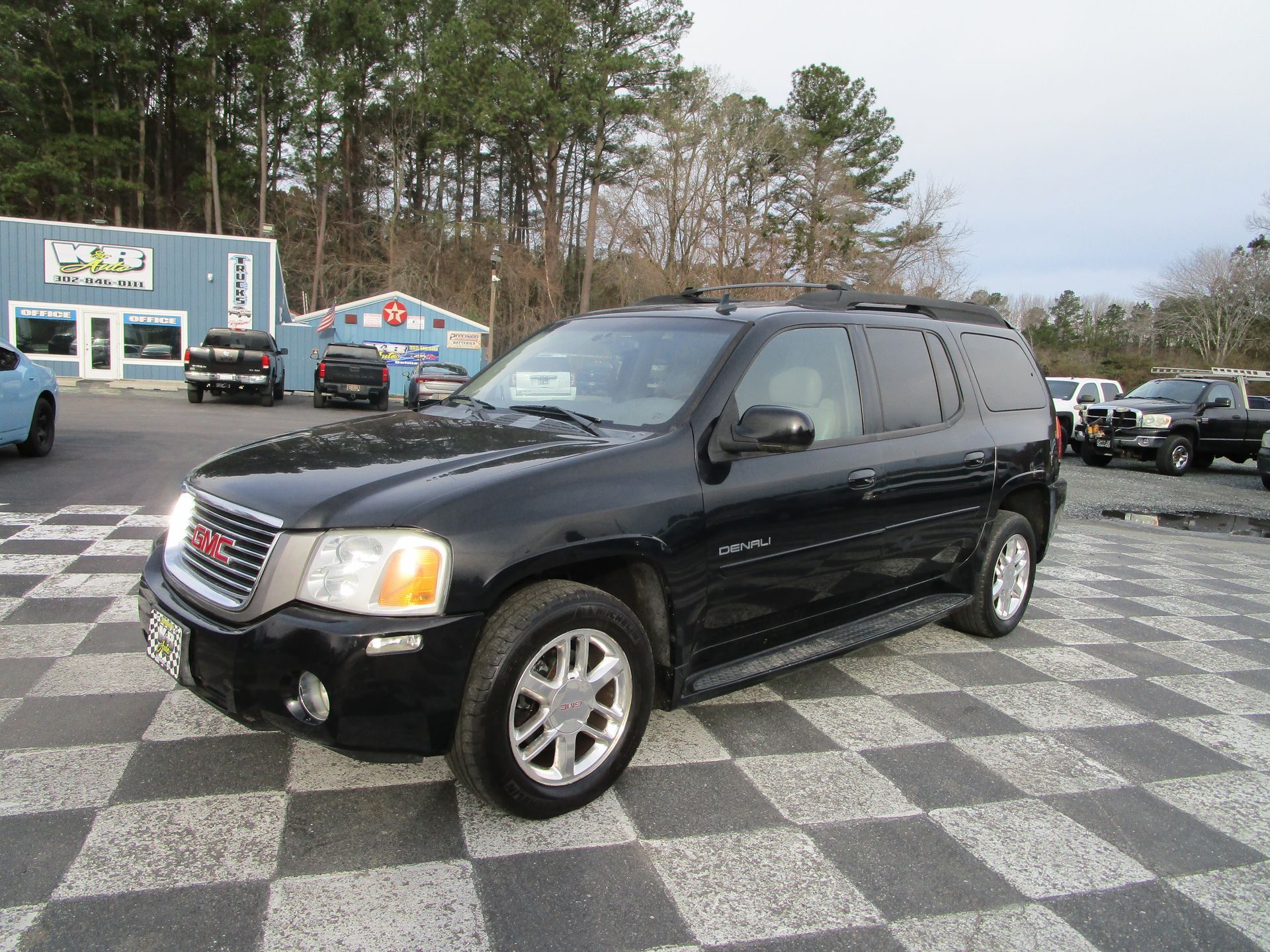 A black GMC Envoy SUV parked on a paved lot with a checkerboard pattern, with a light blue building in the background.