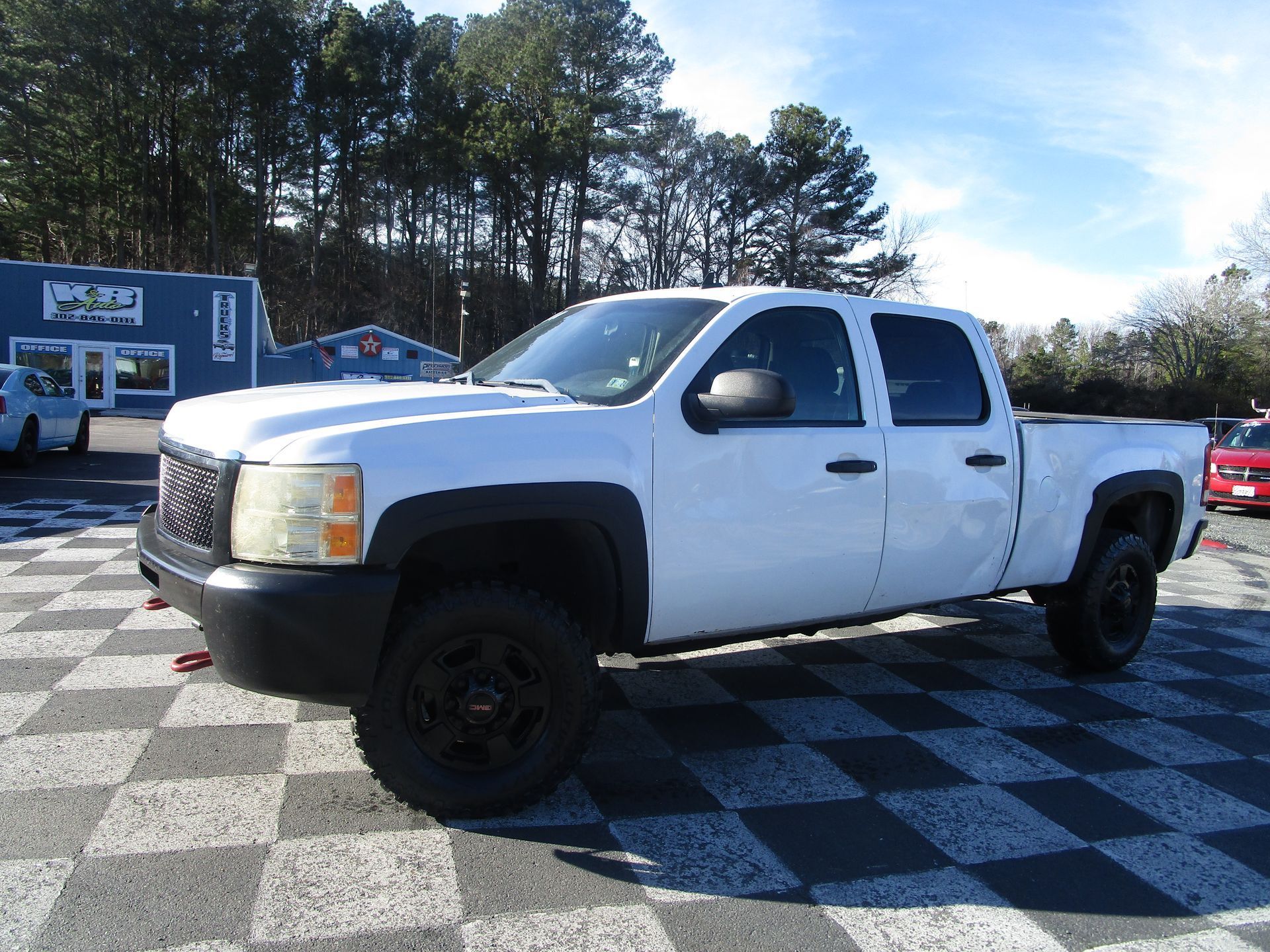 White GMC Sierra pickup truck on a checkered surface, black wheels, parked in front of a building.