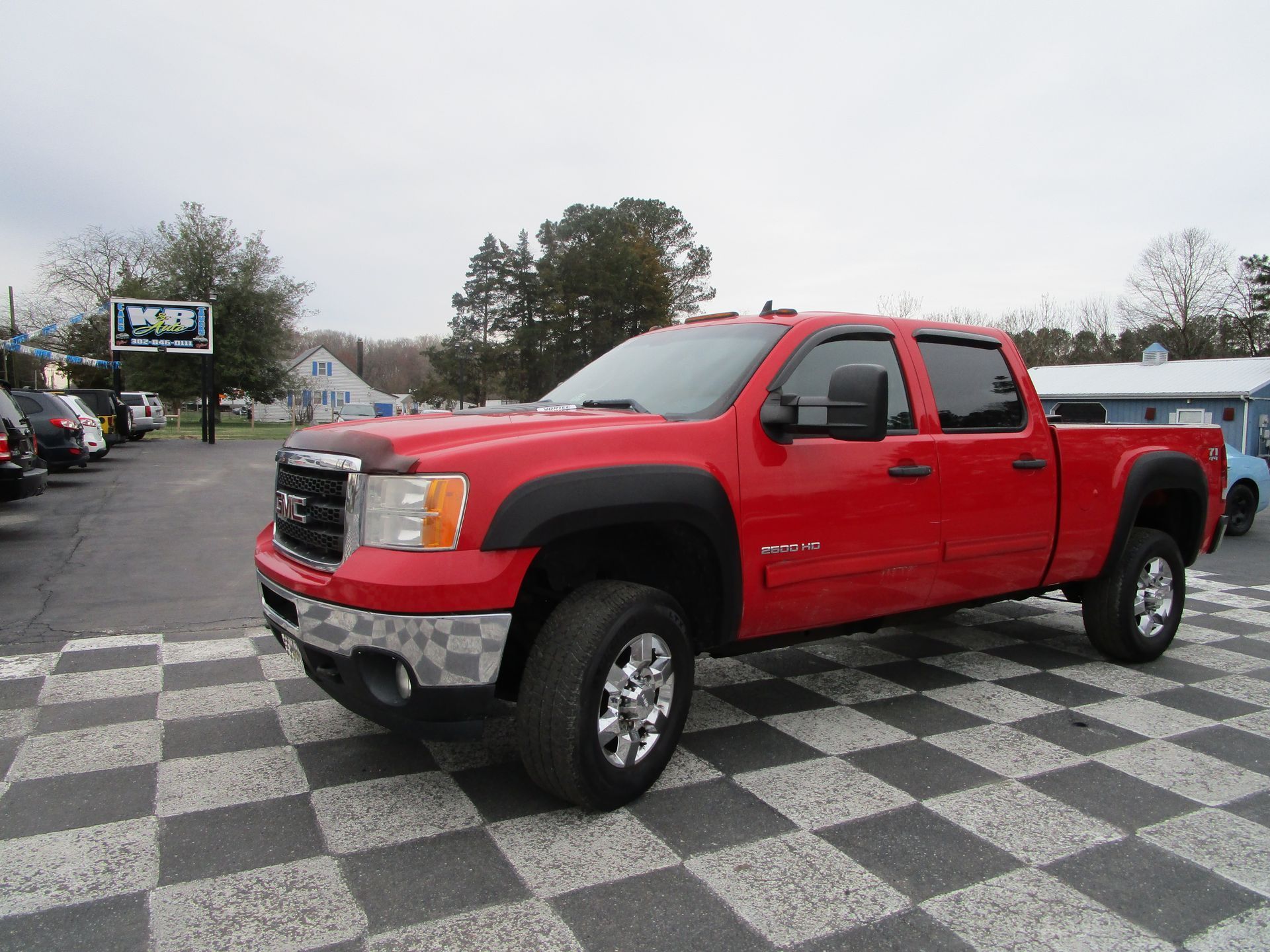 Red GMC pickup truck with black fender flares parked on a checkered lot.