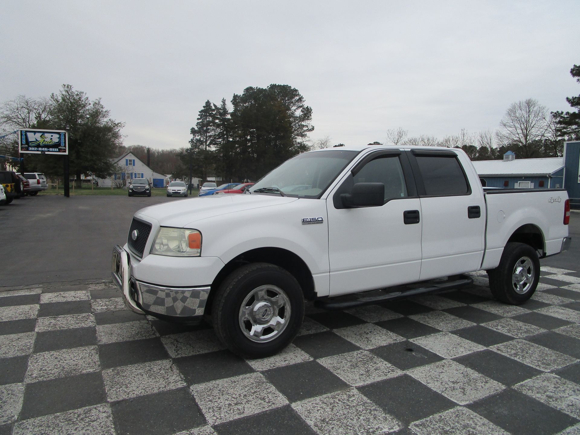 A white Ford F-150 crew cab pickup truck parked on a checkered lot in front of a building.