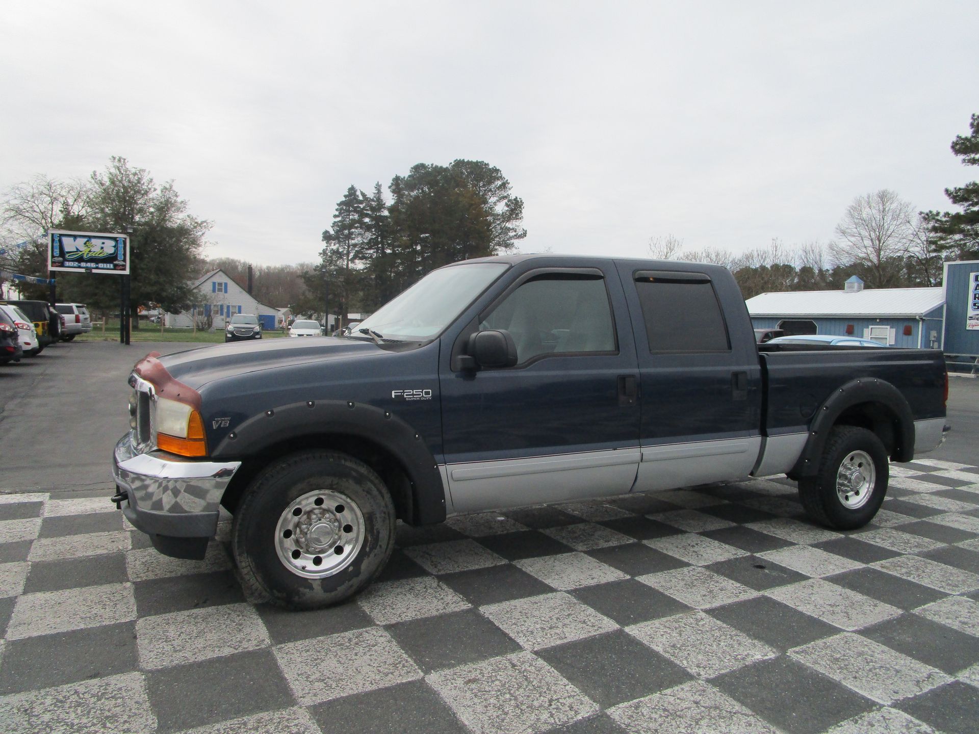 A dark blue Ford Super Duty crew cab pickup truck with two-tone silver lower panels parked on a checkered lot.