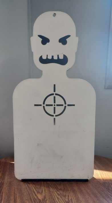 A white target with an angry face and a crosshair on it is sitting on a wooden table.